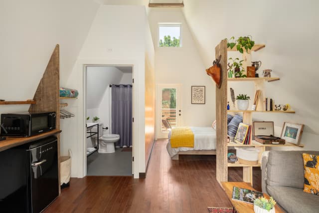 Interior of an A-frame cabin showing the open floor plan: bed, bathroom, living room and coffee bar. Interior of an A-frame cabin showing the open floor plan: bed, bathroom, living room and coffee bar.